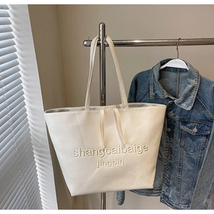 Detail of minimalist beige canvas tote bag with embossed text and long shoulder handles