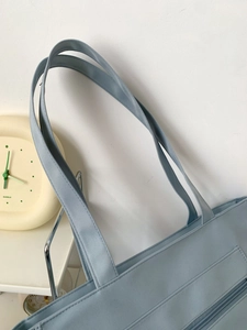 Detailed stitching of light blue canvas tote bag straps and top zipper pocket closure