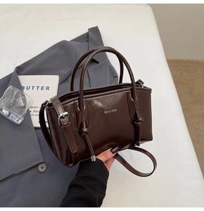 Dettaglio di una borsa tote lucida marrone scuro con doppi manici e nodo in un contesto chic