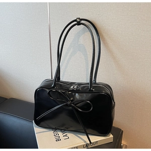 Detail of black patent leather tote bag featuring oversized bow and silver zipper