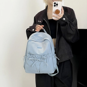 Detail view of a light blue nylon backpack featuring stylish drawstring and bow accents