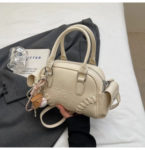 Detail of cream shoulder bag with baseball stitching, letter embossing, and charm