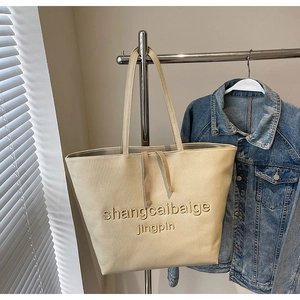 Detail of beige tote bag with embossed text hanging against natural window light