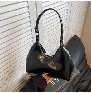 Detail of black glossy croissant bag with silver zipper on minimalist background