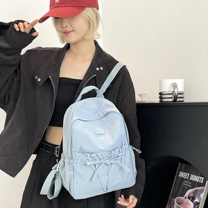Detail of light blue nylon backpack featuring a drawstring bow and side pockets