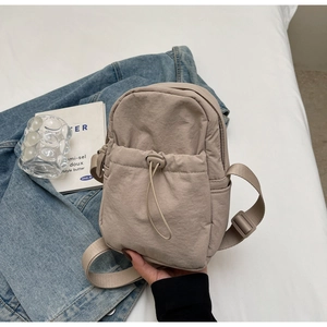 Detail of light beige nylon crossbody bag featuring a drawstring front pocket and strap