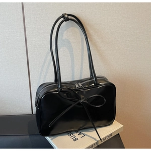 Detailed view of large bow on black glossy patent leather shoulder bag with silver zipper