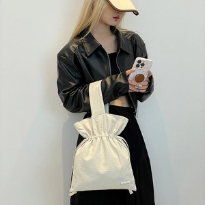 Close-up of minimalist cream nylon drawstring bag with pleated texture and wide strap