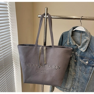 Detail of grey canvas tote bag with embroidered letters on a textured fabric