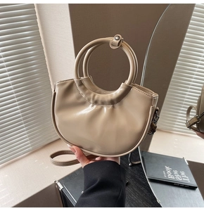 Detail of a beige crescent moon handbag with glossy pleats and circular handles