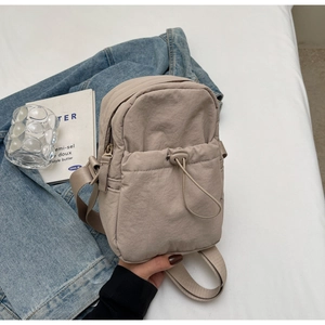 Close-up of lightweight beige nylon crossbody bag with drawstring pocket and zip closure