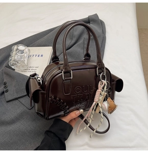Detail of dark brown polished leather bag with embossed letters and baseball charm