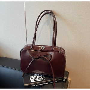 Detail of a burgundy patent leather tote with a bow accent and double zipper closure