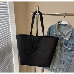 Detail of black canvas tote bag with embossed lettering on a minimalist hanger