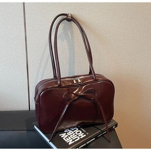 Detail of burgundy patent leather bag with a large bow on a vintage book backdrop