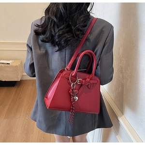 Dettaglio della borsa da sposa rossa con fibbia metallica e nappa a cuore su blazer grigio