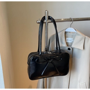 Detail of glossy black shoulder bag featuring a 3D bow design and sleek leather texture