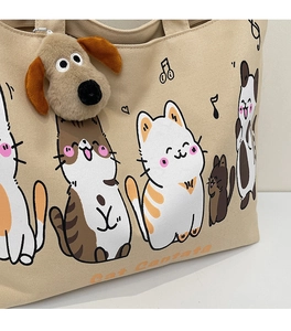 Detail of beige canvas tote with cat illustrations and a plush puppy charm attachment