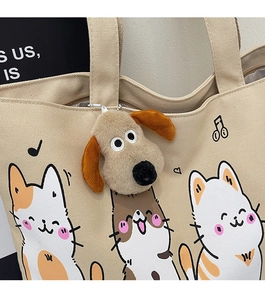 Close-up of beige canvas tote bag with cartoon cat prints and plush puppy pendant