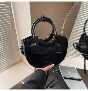 Detailed shot of a black patent leather bucket bag with a round ring handle and long strap
