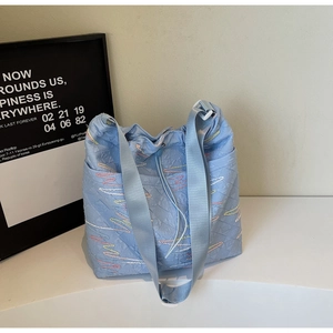 Detail of light blue quilted tote bag with colorful wavy stitching and wide fabric strap
