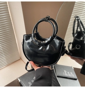 Detail of black patent leather crescent bag with round handle and mirror reflection