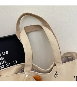 Detail of beige canvas tote with reinforced handles, zip closure and plush charm