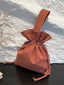 Minimalist rust red nylon drawstring handbag with wide handle on wooden desk