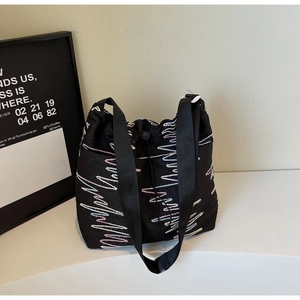 Detail of black canvas tote bag showing wavy colorful embroidery and drawstring closure