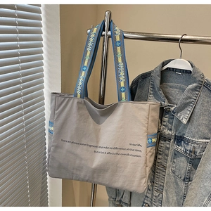 Détail du grand sac cabas gris en toile avec bandoulière rayée bleue et jaune