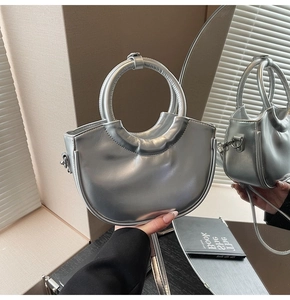 Detail of silver metallic crescent bucket bag featuring a circular top handle and strap