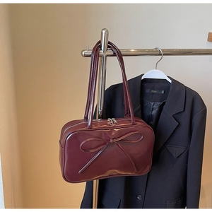 Detailed close-up of dark red glossy leather bag featuring a large bow and double zippers