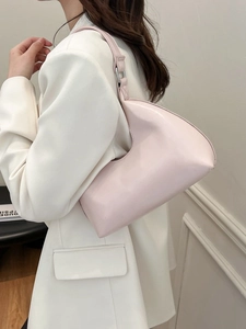 Pink patent leather underarm bag with curved silhouette and silver ring on a white suit