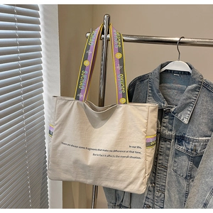 Détail du cabas en toile beige avec bandoulière fleurie et texte sur veste en jean