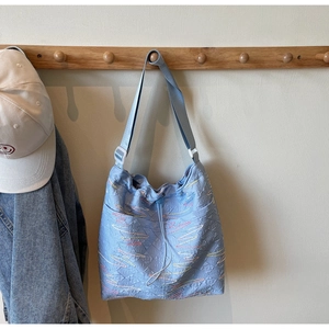 Detail of light blue quilted canvas bucket bag with colorful wavy embroidery and drawstring