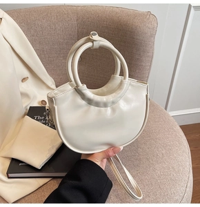 Detail of cream half-moon handbag with circular ring handles and smooth faux leather