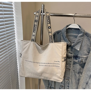 Détail d'un sac fourre-tout en toile beige avec bandoulière trèfle près d'une veste