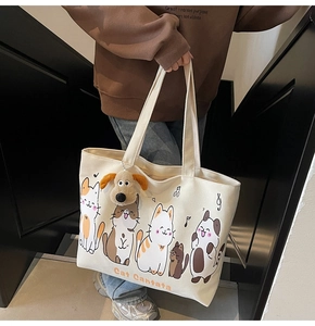 Close-up of cream canvas tote bag featuring cute cat illustrations and a plush dog charm