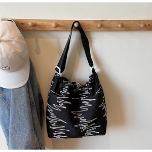 Detail of black canvas drawstring bucket bag with colorful wavy embroidery on strap