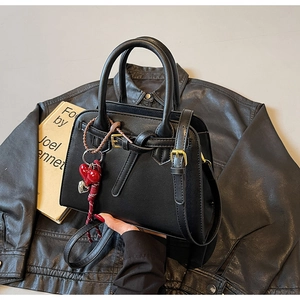 Dettaglio di borsa a tracolla nera chic con ciondolo a cuore rosso e fibbie argentate