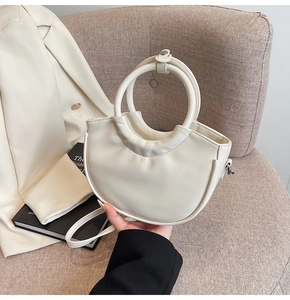 Detail of creamy white crescent handbag featuring a unique round handle and silver hardware