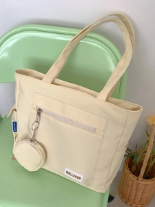 Close-up of beige tote bag with front zipper pocket and round coin purse attachment