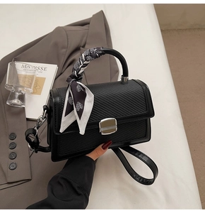 Détail du sac bandoulière noir avec texture tissée, boucle métal et foulard en soie à cœurs
