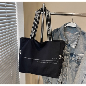 Détail du sac fourre-tout noir montrant la bandoulière tissée et le texte imprimé blanc
