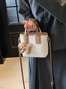 Weiße Leder-Eimertasche mit Sternprägung und braunem Hundeanhänger am Model