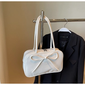 Detail of white glossy shoulder bag featuring a large bow and dual shoulder straps