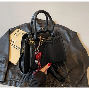 Dettaglio borsa in pelle nera con fibbia dorata e ciondolo a cuore rosso su giacca di pelle
