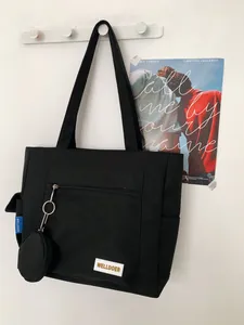 Detail of black canvas tote bag with front zipper pocket and round hanging coin purse