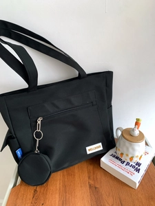 Detail of black canvas tote bag with front zipper pocket and round hanging coin purse