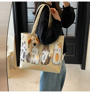 Detail of beige canvas tote bag with cartoon cat prints and plush dog charm on shoulder